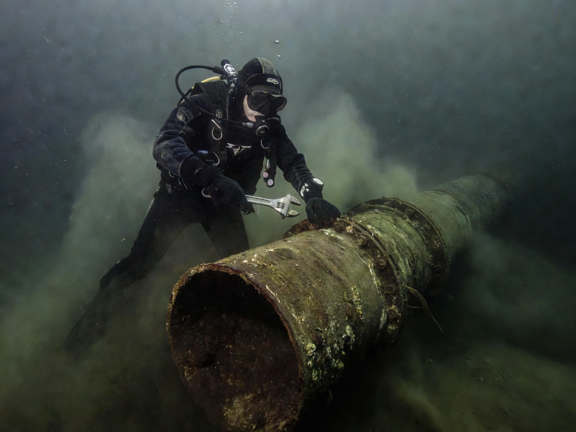 Diver performing maintenance on an underwater pipe structure in murky water